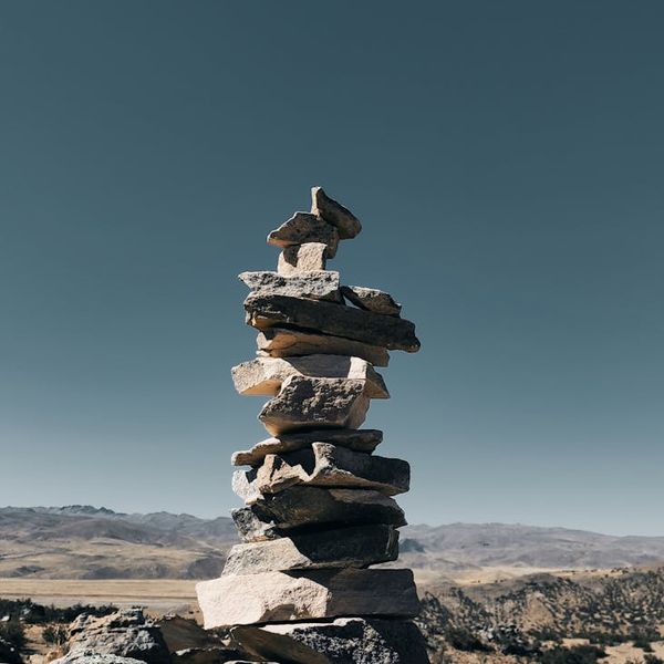A balanced stack of dark stones against a teal and black background, symbolizing harmony.