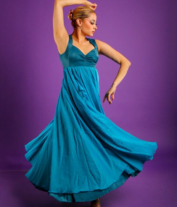 Woman performing a fluid cardio movement in a calm, dark studio with teal light accents.